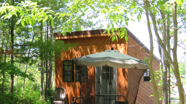 A wooden cabin with a covered patio area, a table, and two chairs.