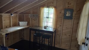A small wooden cabin with a kitchenette, a window with curtains, and a mirror on the wall.