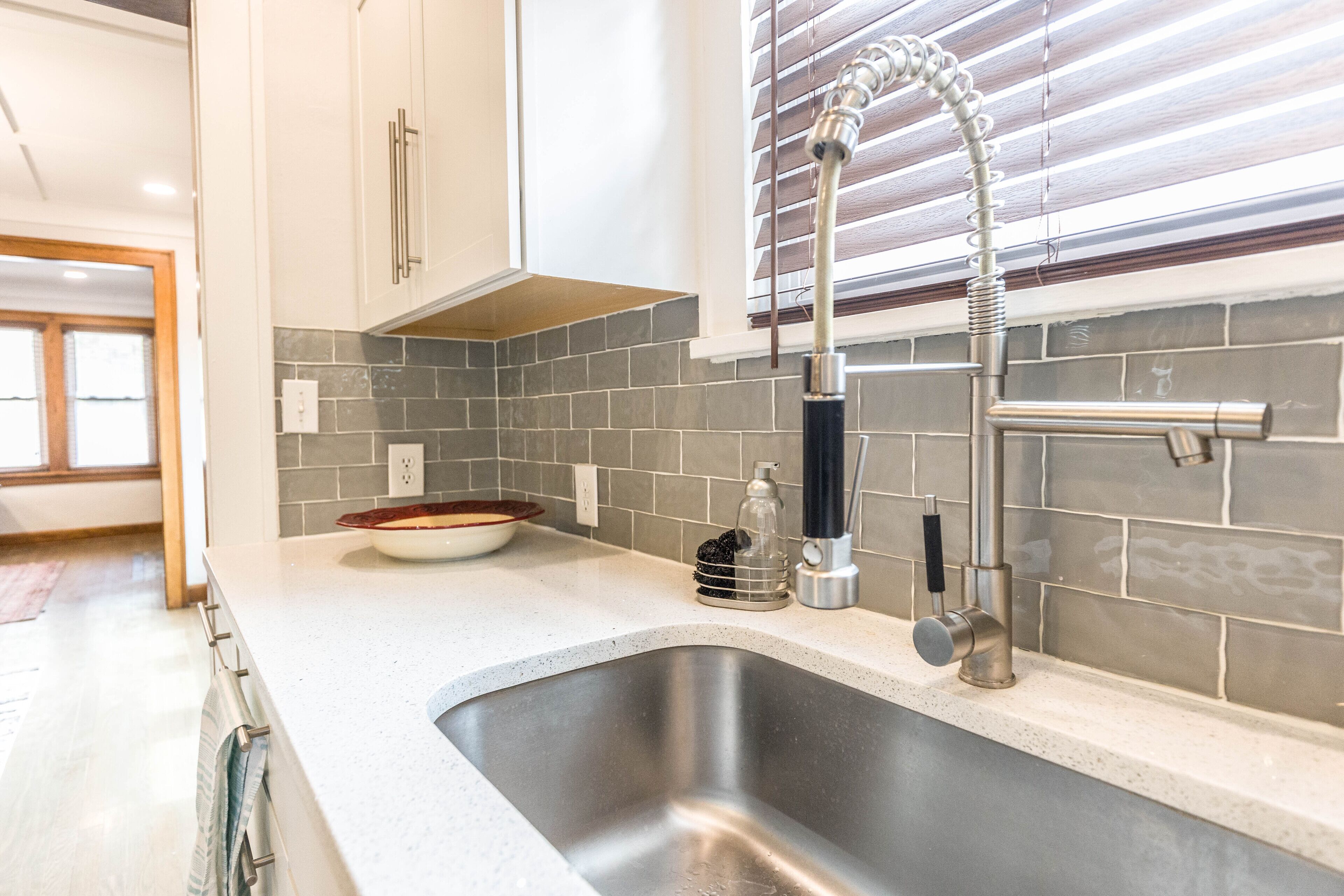A kitchen with a stainless steel sink, a modern faucet, and a tiled backsplash.
