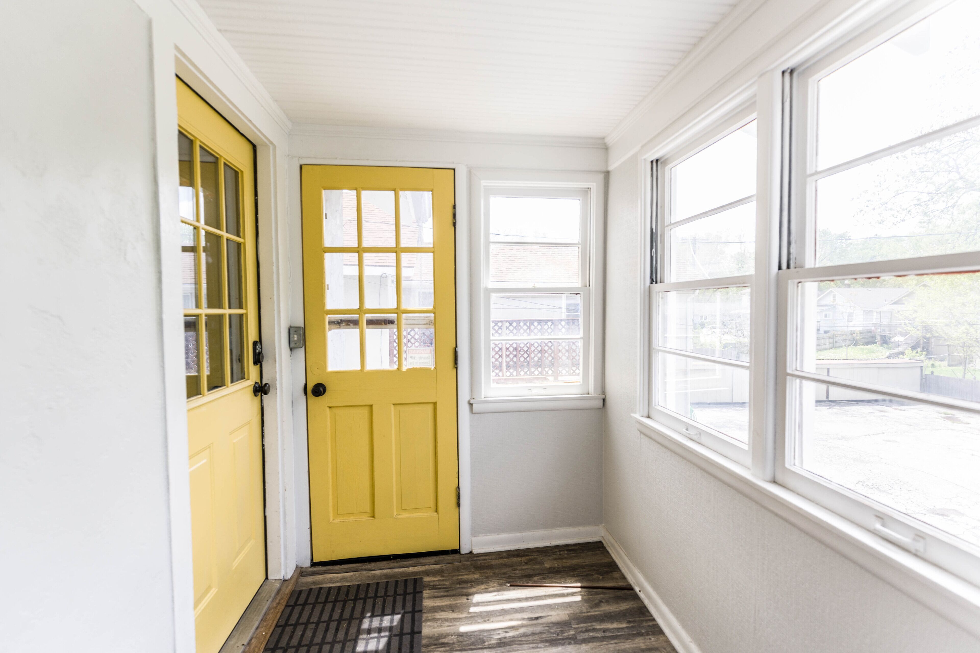 A yellow door with a window, a white wall, and a window with a view of the outside.