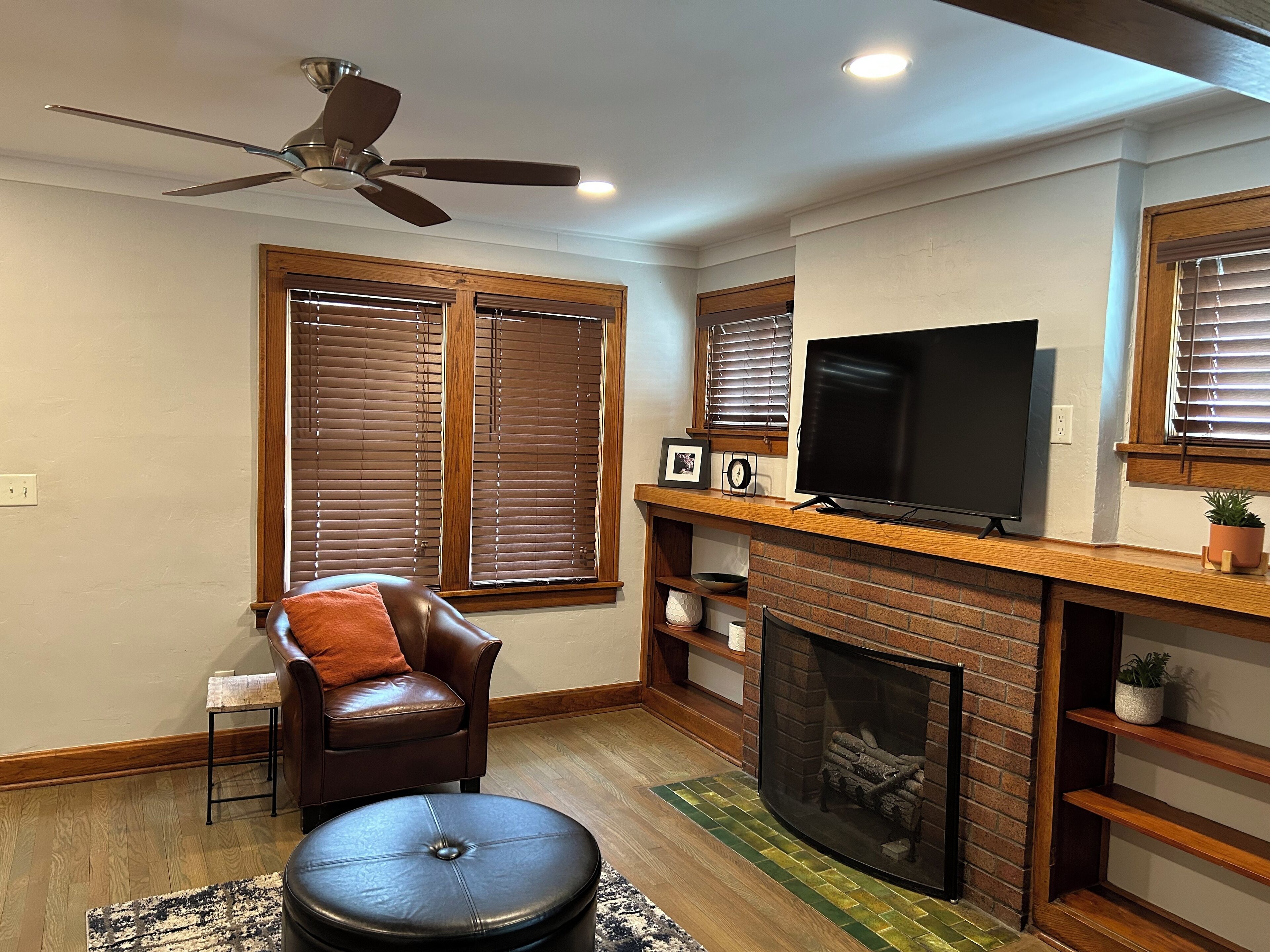 Ein Wohnzimmer mit Kamin, Fernseher, Deckenventilator und braunem Ledersessel.