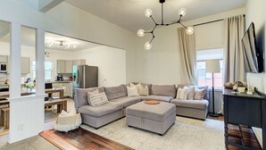 Ein modernes Wohnzimmer mit einem grauen Ecksofa, einem Holztisch und einem großen Fenster mit Vorhängen.