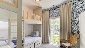 Ein Zimmer mit Etagenbetten, einem Sessel und einem fenster mit Vorhängen.