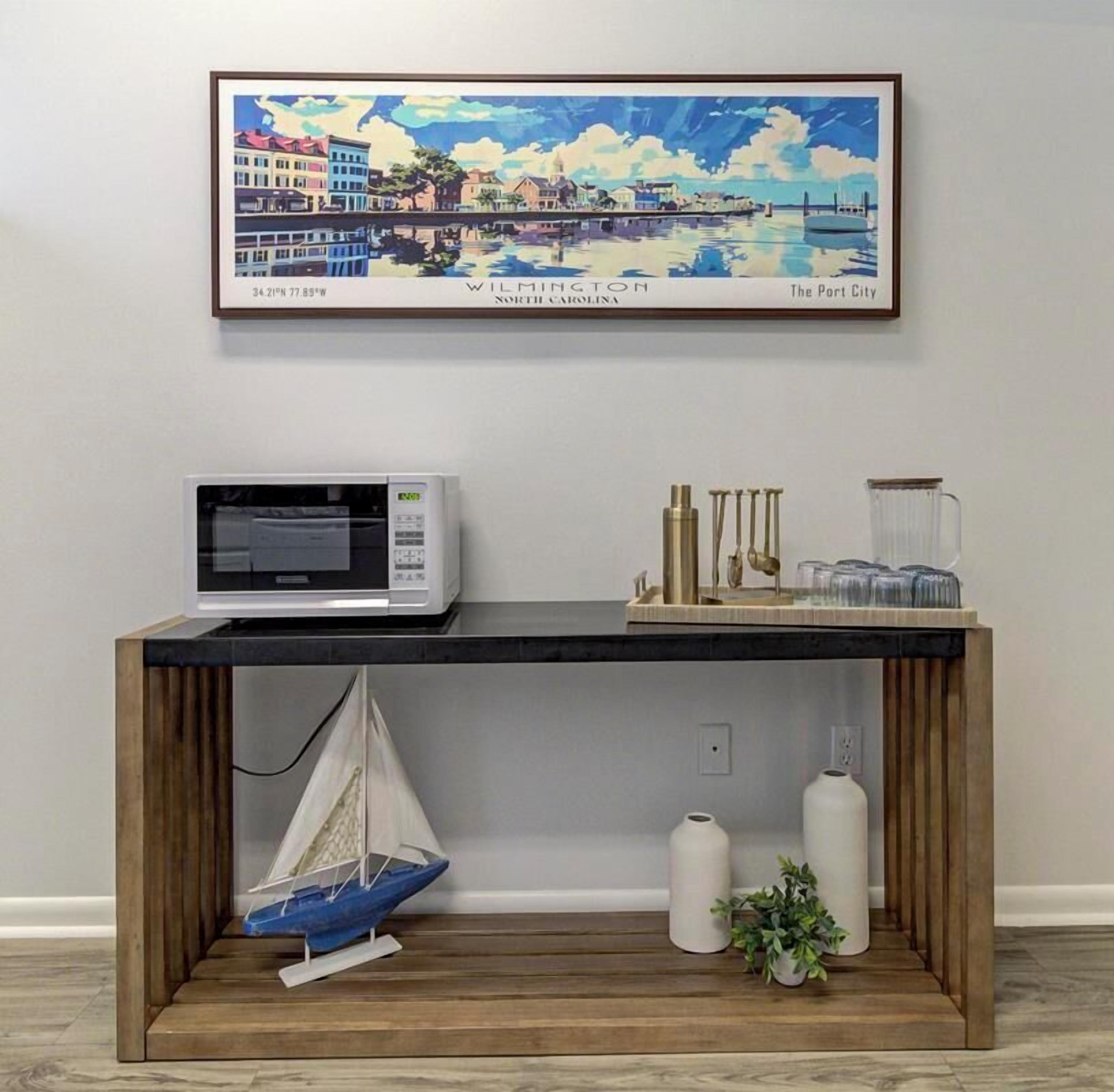 A wooden console table with a microwave, decorative items, and a small sailboat model.