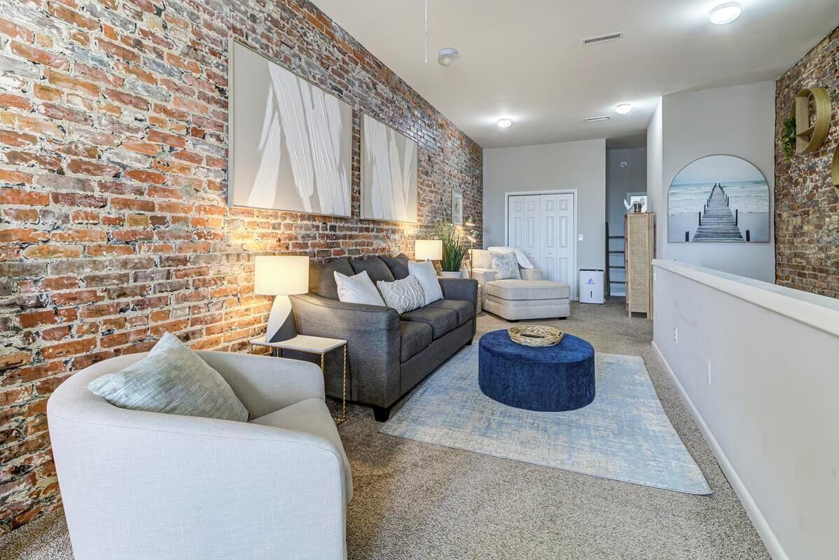 A living room with a brick wall, a grey sofa, a white armchair, and a blue ottoman.