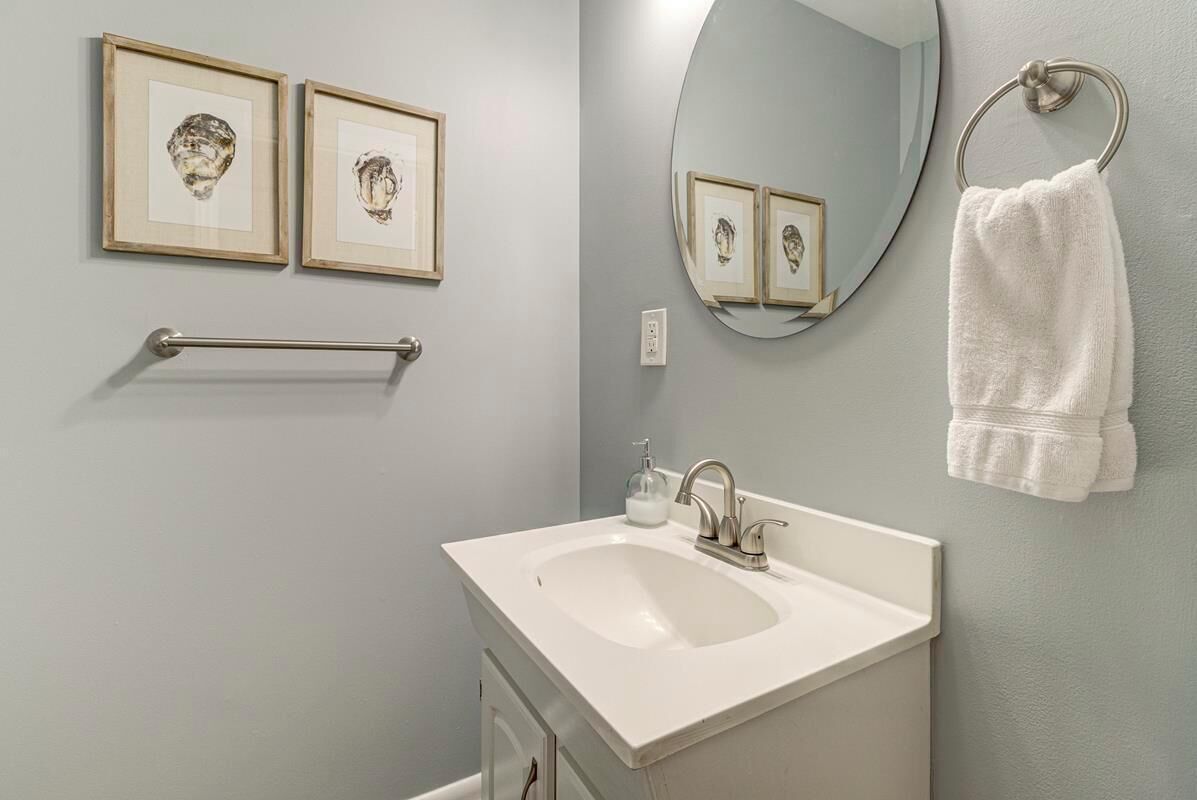 A bathroom with a white sink, framed artwork on the wall, a towel ring, and a mirror.