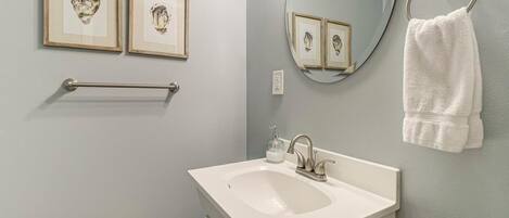 A bathroom with a white sink, framed artwork on the wall, a towel ring, and a mirror.