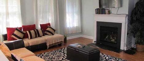 Una sala de estar con un conjunto de sofá, una chimenea, un televisor y una alfombra estampada.