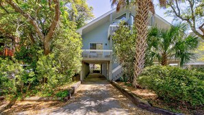 A two-story building with a balcony, surrounded by lush greenery and trees. - Kure Beach Treehouse | Walk to Beach | Sleeps 8 (Kure Beach)