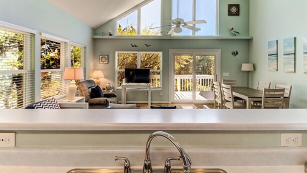 A kitchen with a large island, a dining area with a table and chairs, and a ceiling fan. - Kure Beach Treehouse | Walk to Beach | Sleeps 8 (Kure Beach)