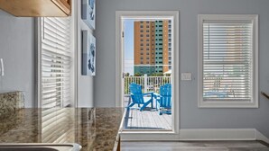 Une cuisine dotée d’un plan de travail en granit, d’un évier et d’une porte donnant sur un balcon avec des chaises bleues et une vue sur un immeuble imposant.