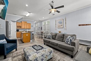 Una sala de estar con un sofá gris, un sillón azul, una mesita de centro y un ventilador de techo.