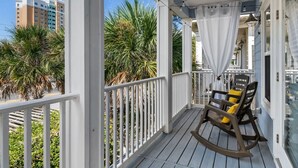 Une terrasse en bois avec une chaise berçante et une balustrade blanche.