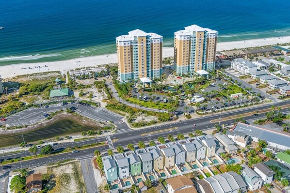 Un complejo hotelero frente al mar con varios edificios altos, una playa y un estacionamiento.