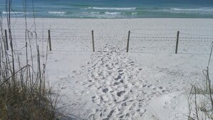 Une plage de sable avec des empreintes menant à l’eau, une clôture et une végétation clairsemée.