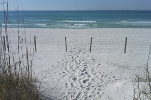 A sandy beach with footprints leading to the water, a fence, and sparse vegetation.