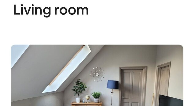 Ett vardagsrum med ett sluttande tak, en soffa, ett soffbord, ett TV-bord, en lampa och en växt.
