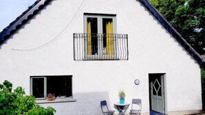 Ett vitt hus med en balkong, ett litet bord med stolar och en dörr.