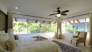 Un dormitorio con una cama grande, un ventilador de techo, una silla y vistas a zonas verdes.
