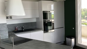 A modern kitchen with white cabinets, a stainless steel oven, and a large window. - Appartement Idéal Découverte Landes Pays Basques (Tarnos)