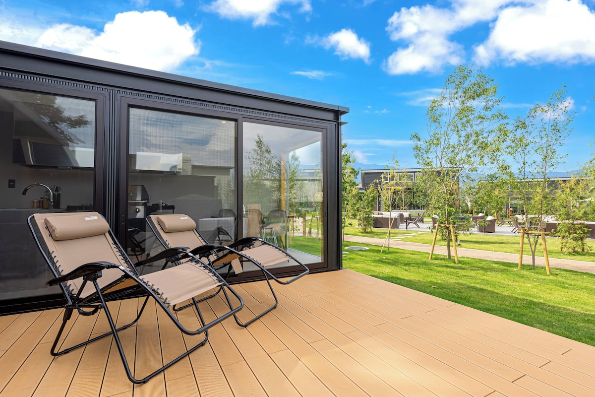 A modern outdoor deck with two lounge chairs and a glass-enclosed patio area.