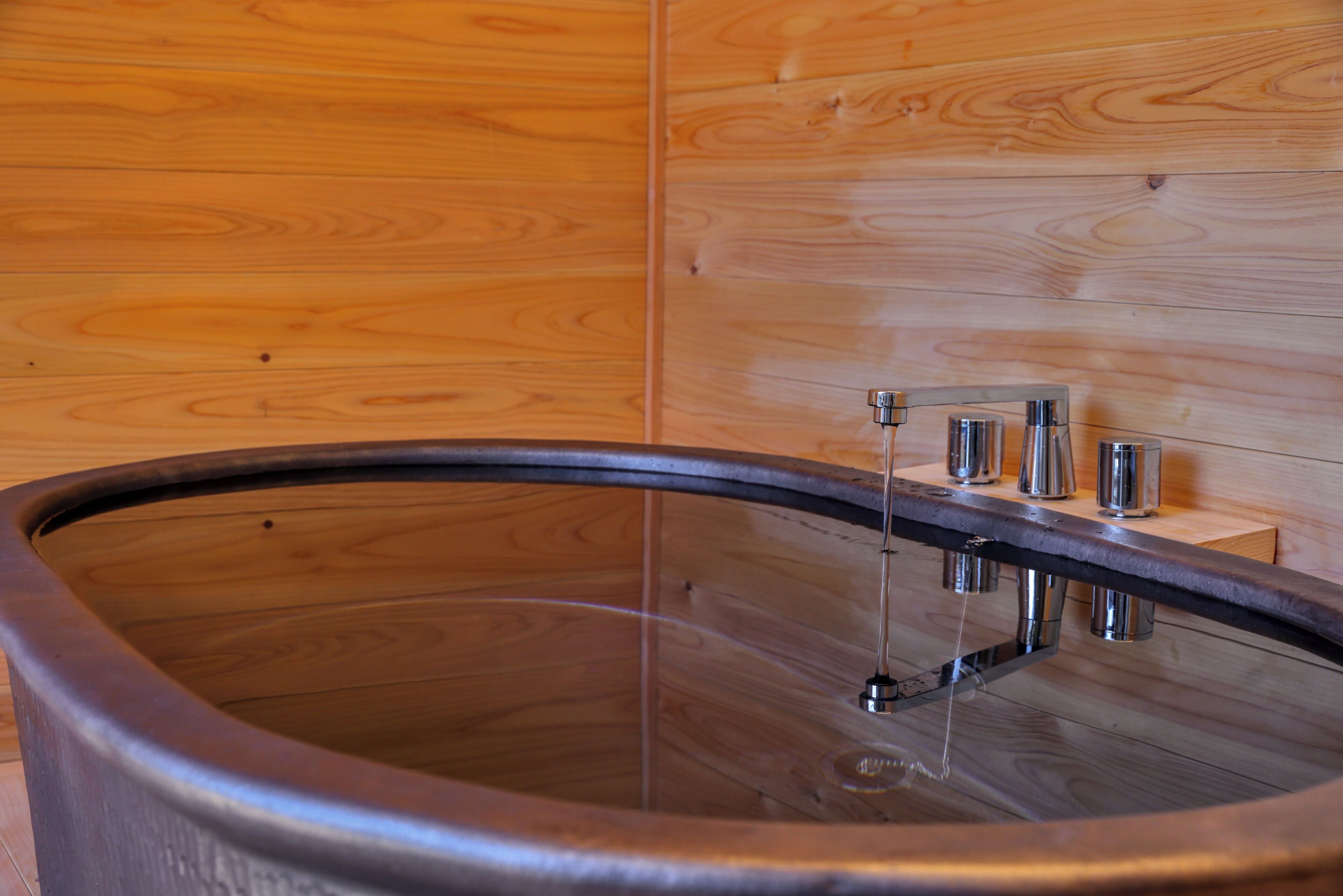 Een houten interieur met een groot bad en een klein plankje met twee metalen bakken.