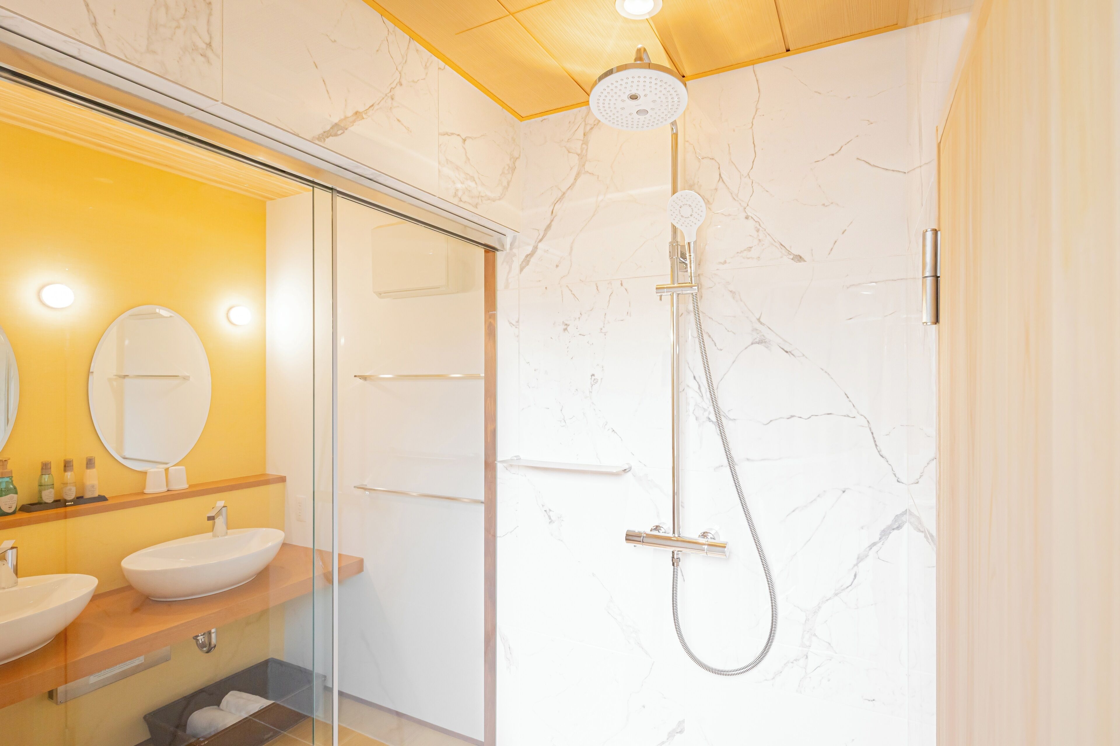 A modern bathroom with a glass-enclosed shower, marble walls, and a vanity with two sinks.