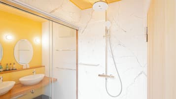 A modern bathroom with a glass-enclosed shower, marble walls, and a vanity with two sinks.