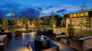 Un espace extérieur aménagé en terrasse, avec un foyer, des sièges et un bâtiment moderne en arrière-plan.