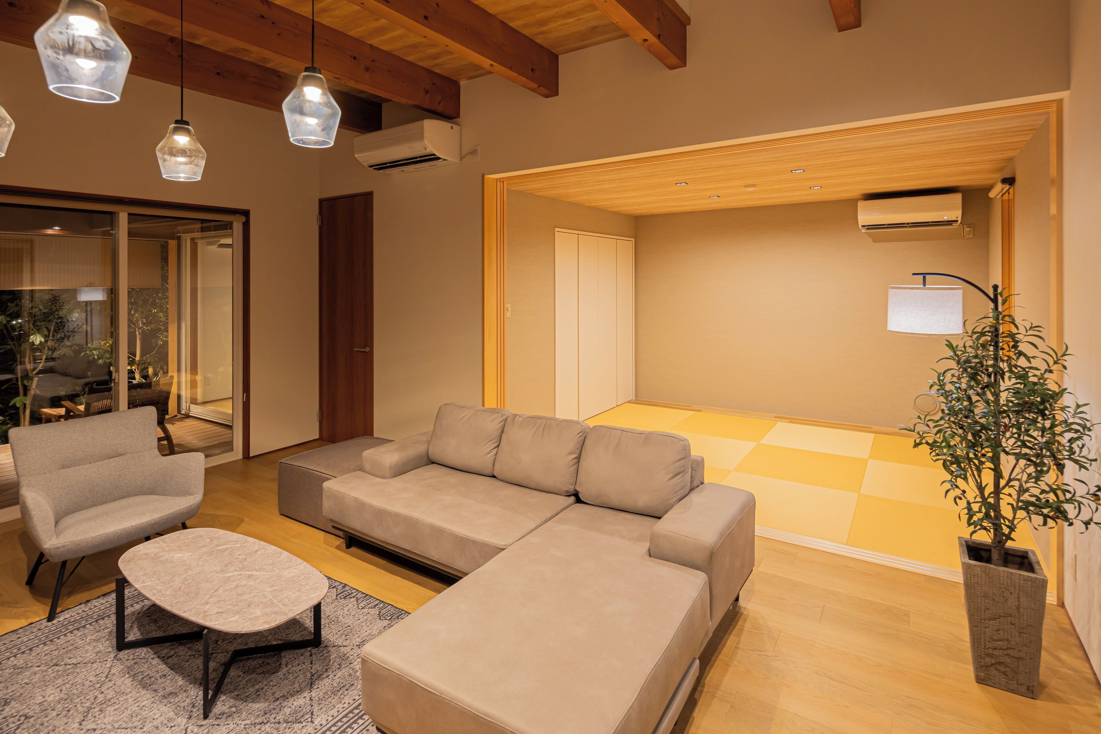 A modern living room with a sectional sofa, armchairs, and a coffee table. There is a large window with a view of greenery outside.