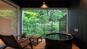 Une pièce dotée d’une grande fenêtre, d’un jacuzzi, d’une chaise en bois et d’une petite table.