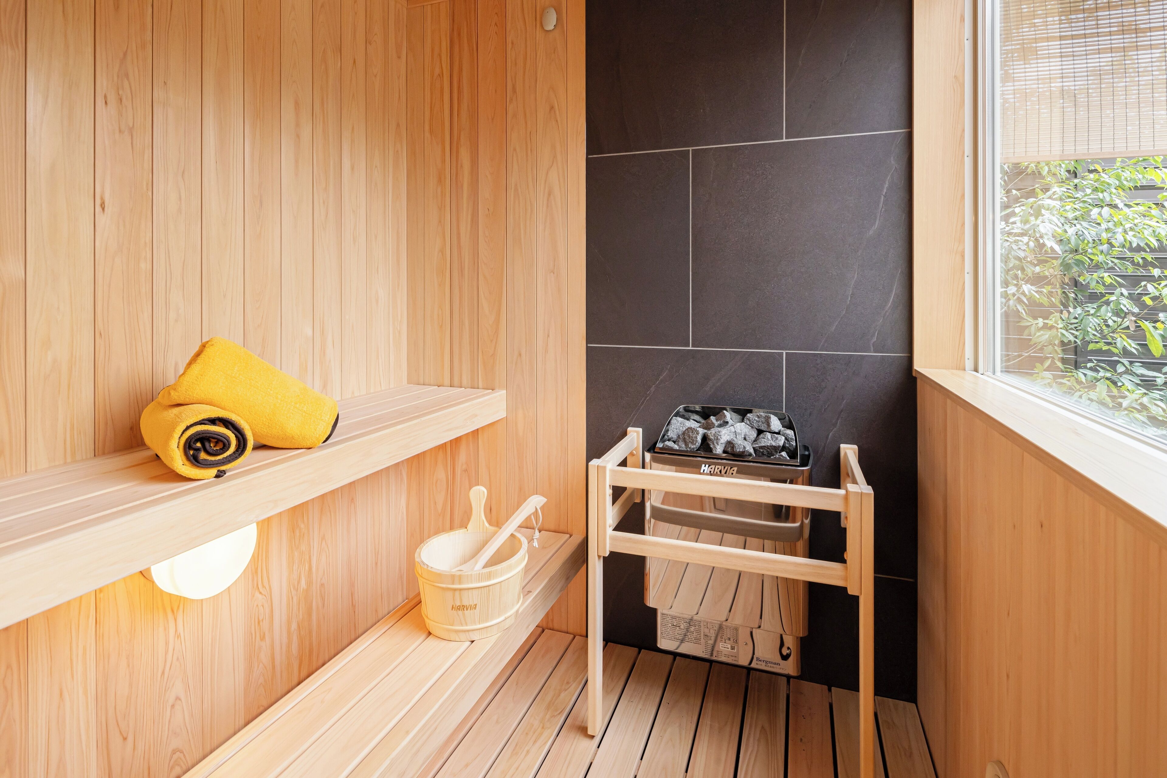 Um salão de sauna de madeira com uma prateleira contendo uma toalha amarela, um balde de madeira com uma concha e um banco de sauna.