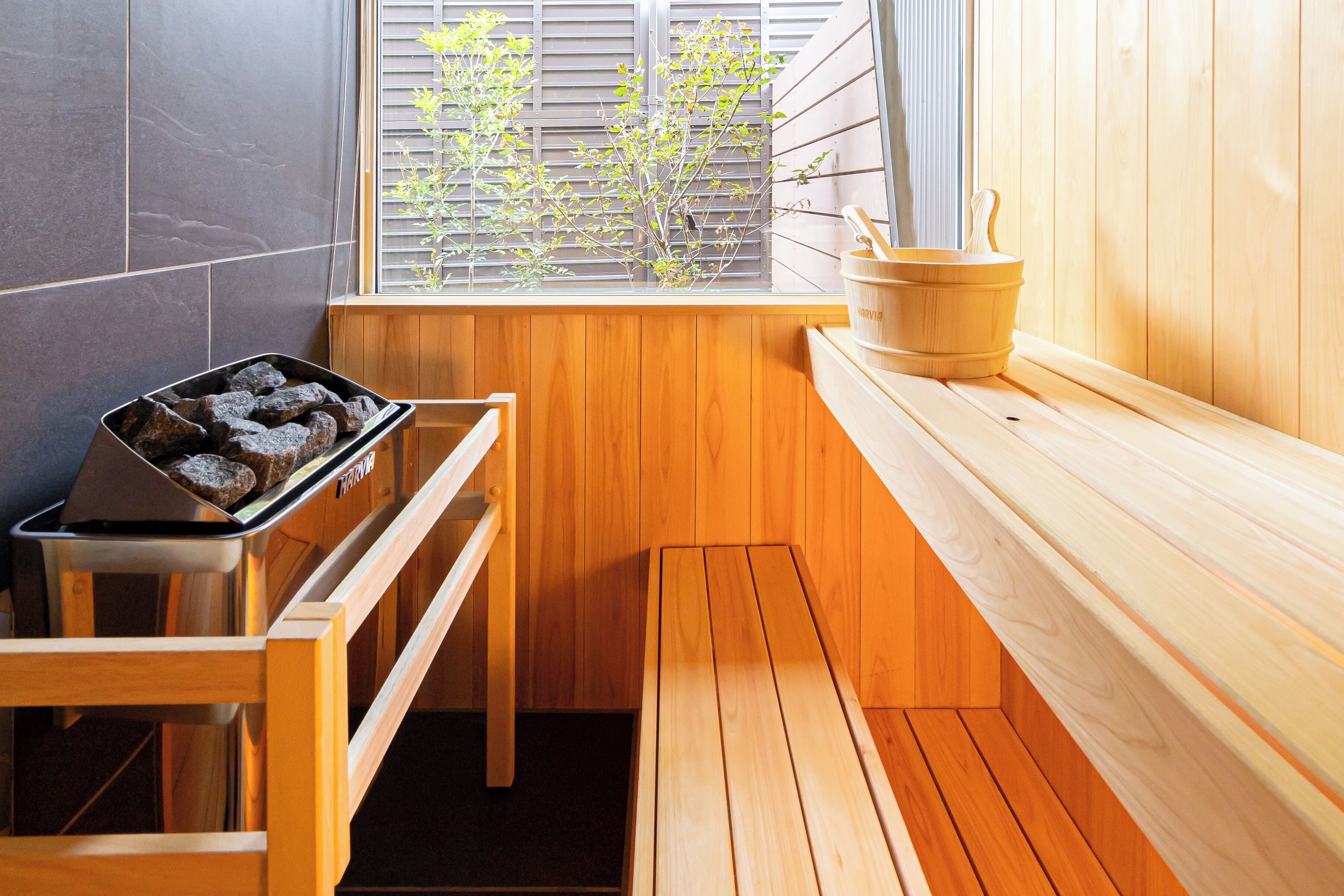 Un sauna con un banco de madera, un recipiente metálico con piedras y un cubo de madera sobre una repisa.
