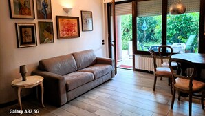 Ein Wohnzimmer mit braunem Ledersofa, einem kleinen Beistelltisch und einem Essbereich mit Tisch und Stühlen. Sechs gerahmte Kunstwerke sind an der Wand angebracht.