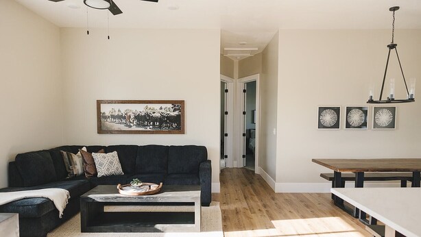 A living room with a dark sofa, a coffee table with a tray, a white rug, and a wooden dining table with benches. - COW PALACE 
Experience Rustic Charm and Tranquility at our Old Milk Barn.  (Preston)