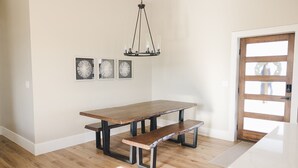A dining area with a wooden table and bench, a chandelier, and three wall-mounted pictures. - COW PALACE 
Experience Rustic Charm and Tranquility at our Old Milk Barn.  (Preston)
