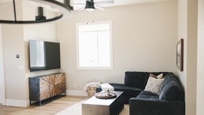 A modern living room with a dark sofa, a coffee table, and a flat-screen TV mounted on the wall. - COW PALACE 
Experience Rustic Charm and Tranquility at our Old Milk Barn.  (Preston)