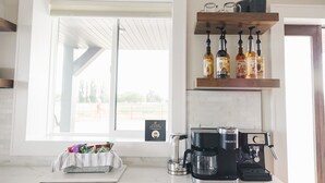 A kitchen with a coffee maker, a Keurig machine, and a shelf with bottles. - COW PALACE 
Experience Rustic Charm and Tranquility at our Old Milk Barn.  (Preston)