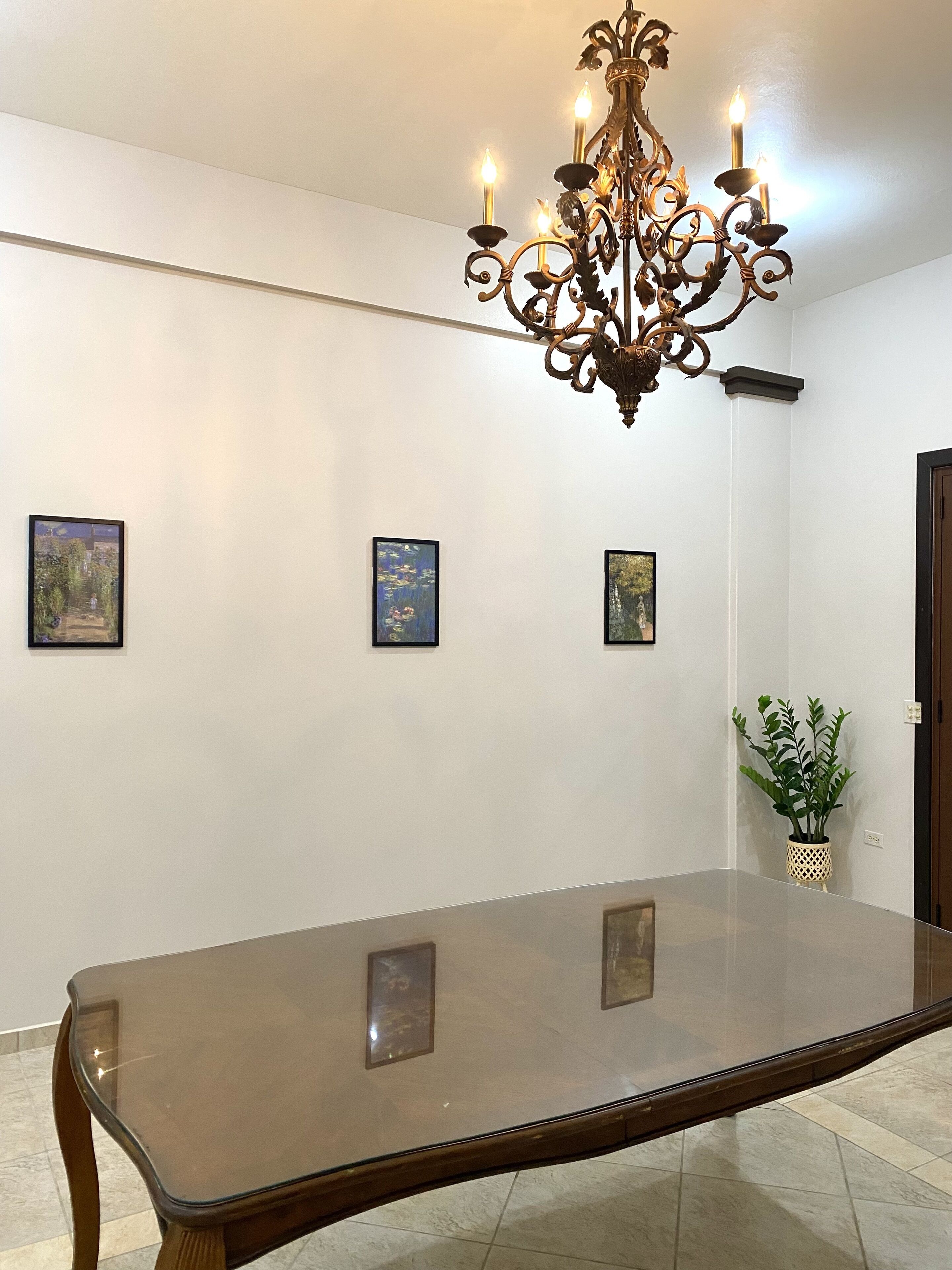 A dining area with a long table, a chandelier, and three framed artworks on the wall.