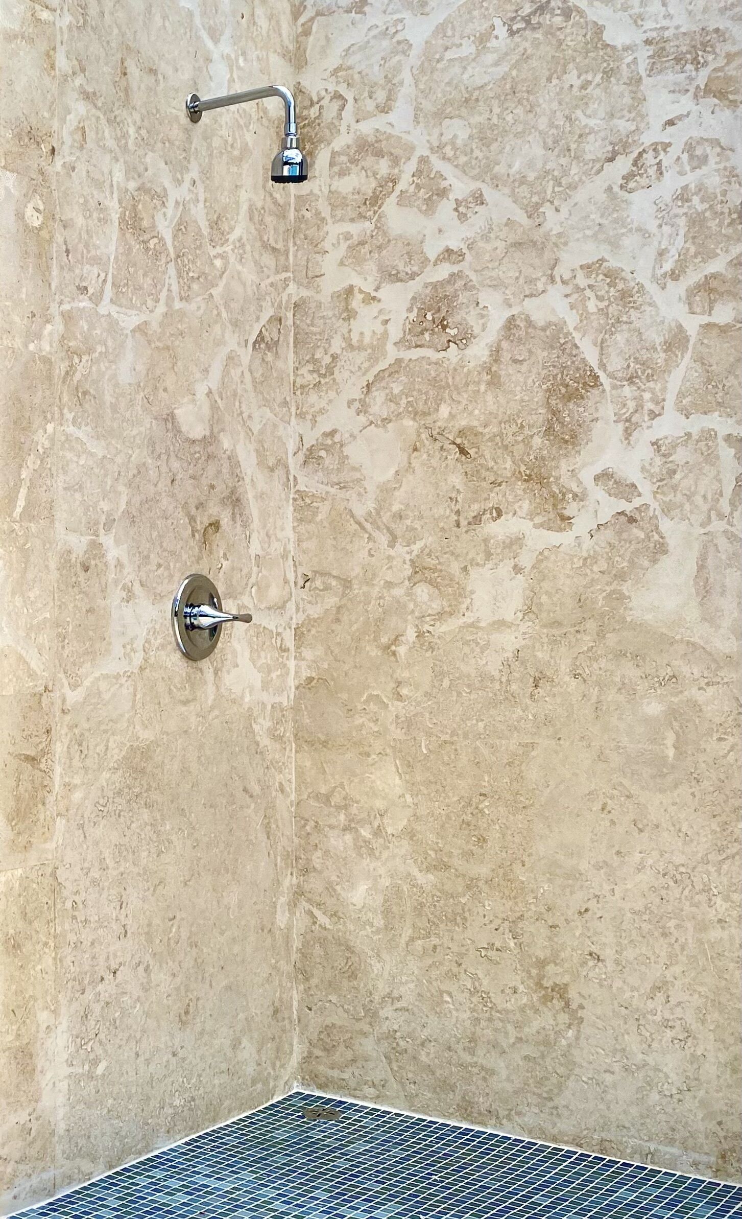 A bathroom with a stone wall, a shower head, and a tiled floor.