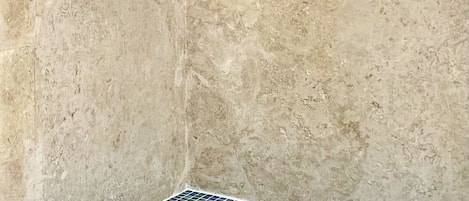 A bathroom with a stone wall, a shower head, and a tiled floor.