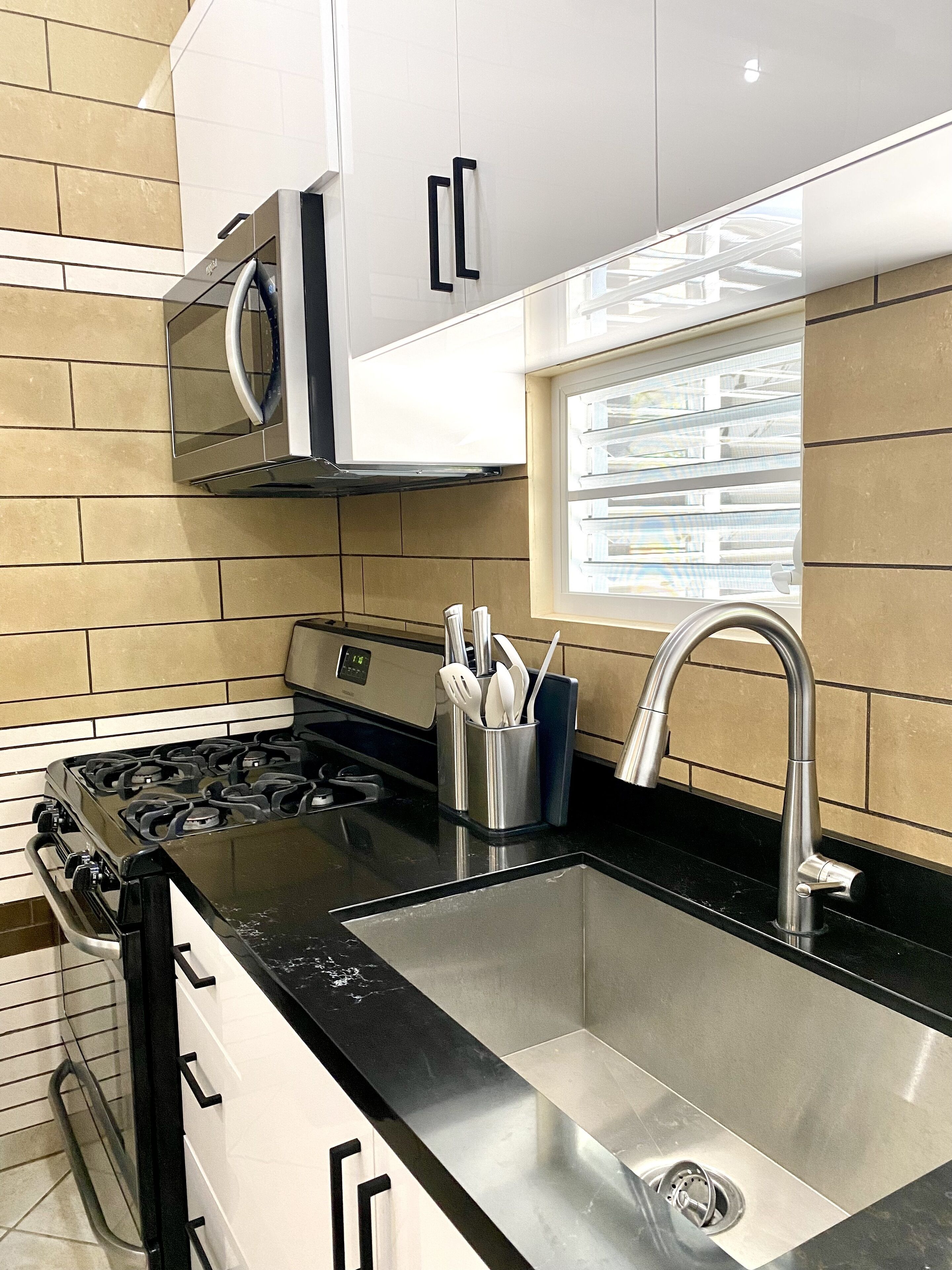 A modern kitchen with a gas stove, stainless steel sink, and white cabinets.