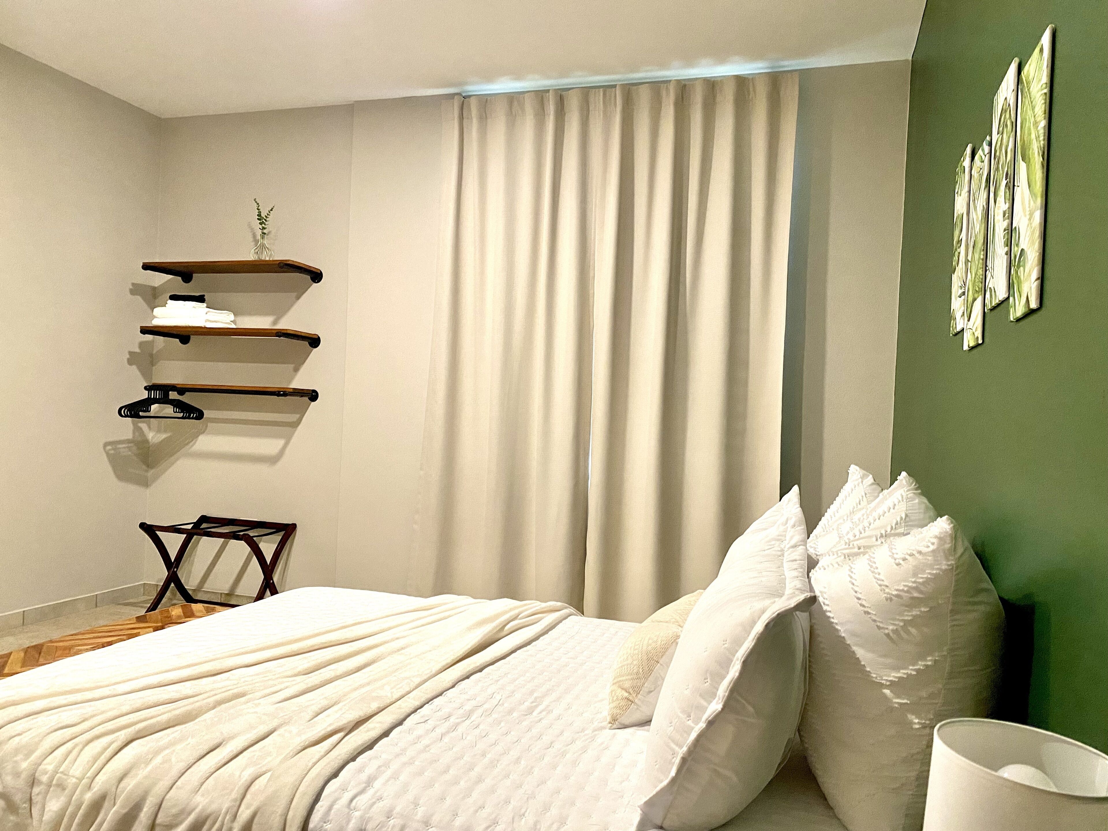 A bedroom with a bed, a hanging shelf with clothes, a bedside table, and a green wall.