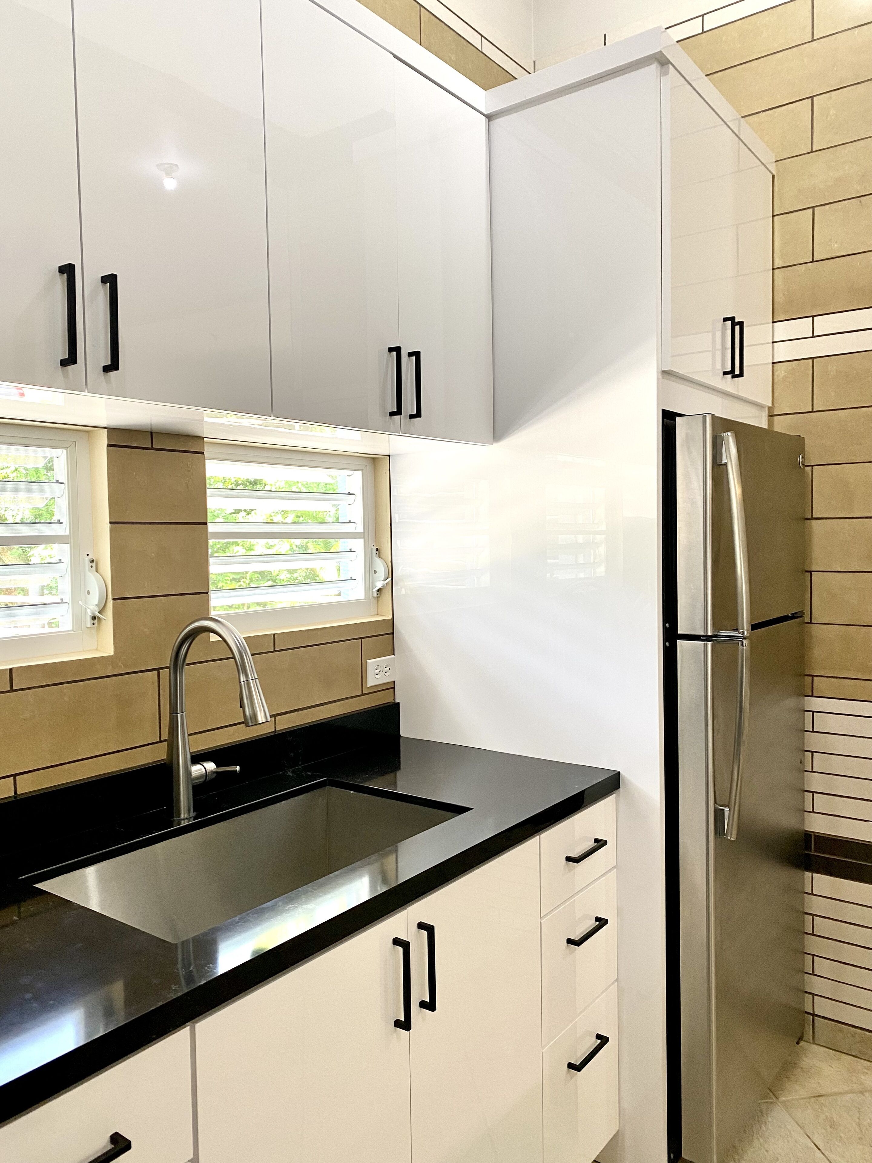 Una cocina moderna con armarios blancos, un refrigerador de acero inoxidable y una encimera negra.