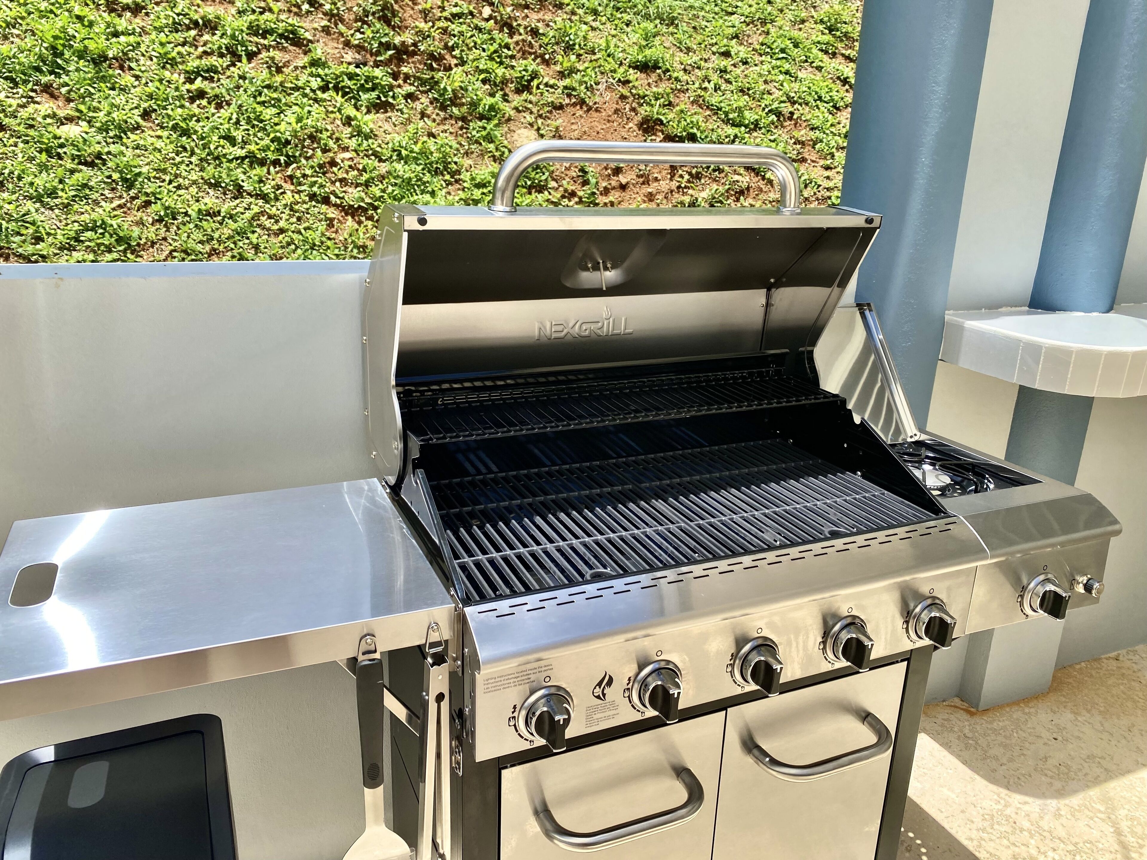 En udendørs grill i rustfrit stål med fire brændere og en sidebrænder, mærket 'NEWGRILL'.