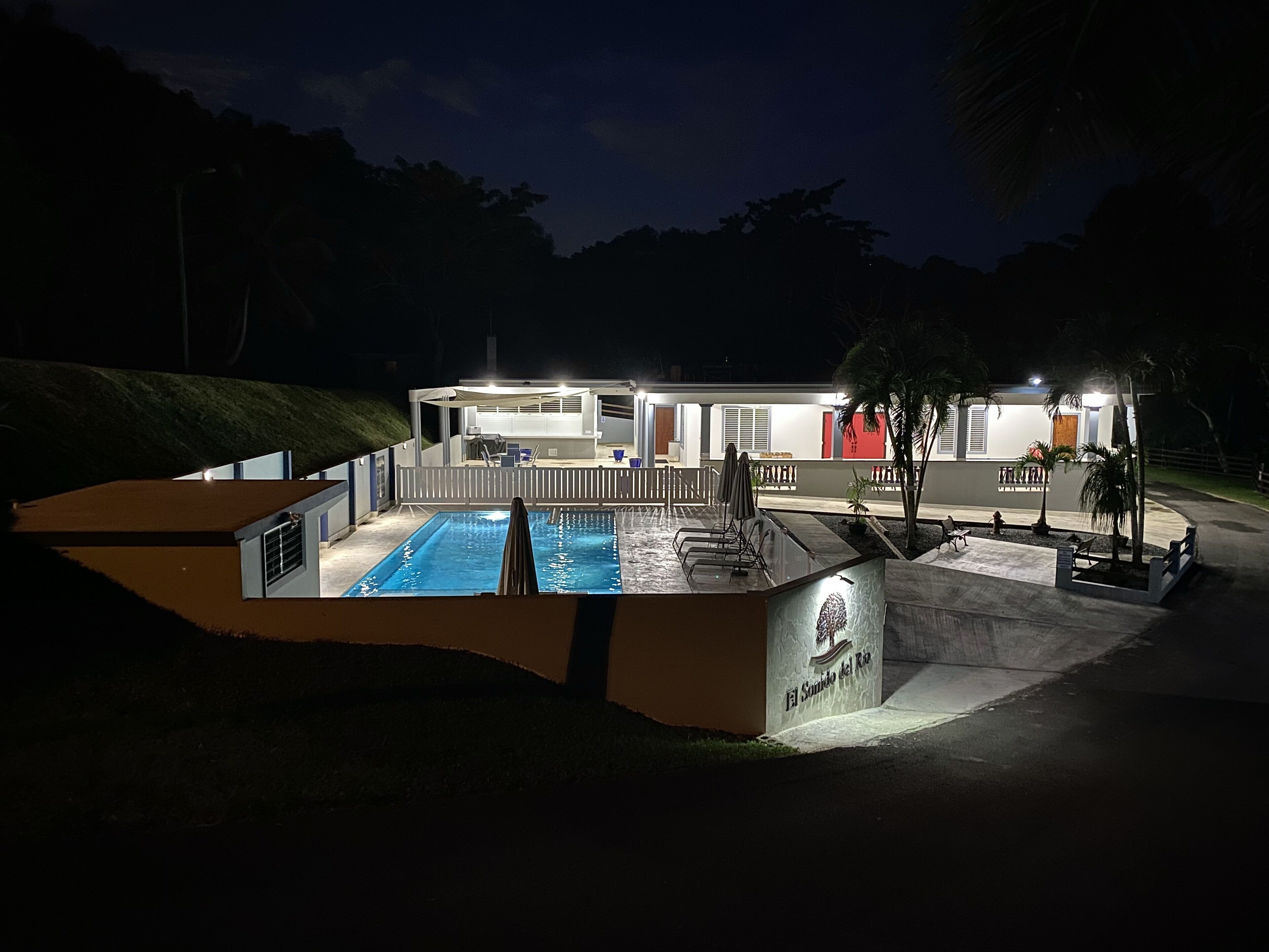 A modern hotel with a swimming pool, outdoor seating, and a well-lit entrance.