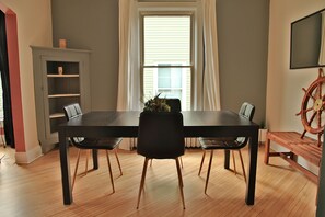 Zona pranzo con tavolo e sedie neri, pavimento in legno, finestra con tende, libreria e decorazione a forma di timone di nave.