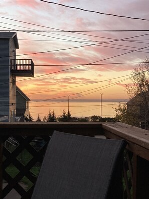 Un balcone con vista sul tramonto riflesso sull'acqua, linee elettriche e un edificio con un balcone.