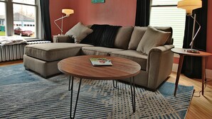 Una sala de estar moderna con un sofá seccional, una mesa de centro redonda y dos lámparas de pie.