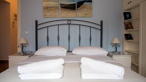Een net opgemaakt tweepersoonsbed met witte lakens en handdoeken, een zwarte metalen hoofdbord en een muur met een schilderij van een strandlandschap.